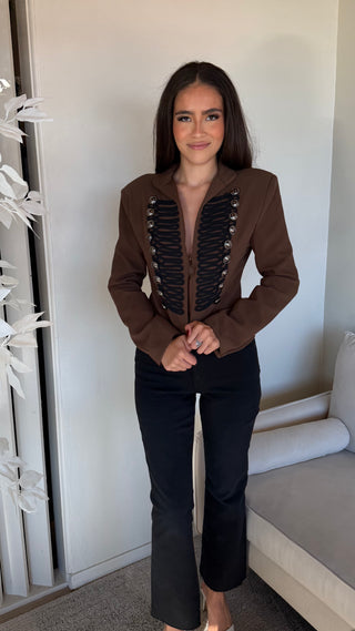 Olive brown cropped jacket with shoulder pads and button details worn by a model.
