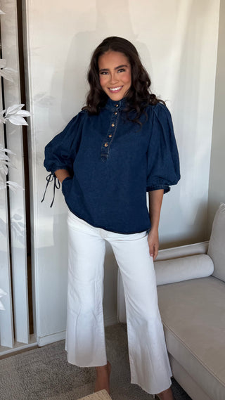 Navy denim top with puff sleeves and button front, worn by a model with white trousers.