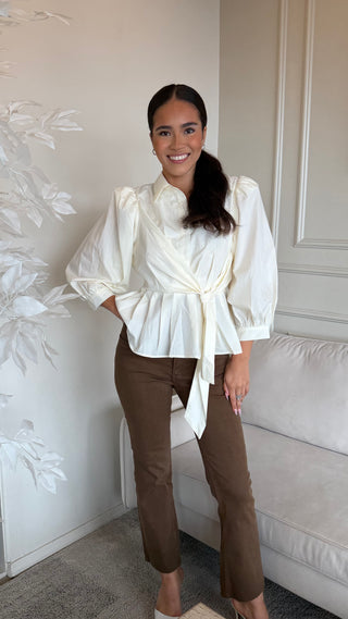 A cream blouse with tie waist and puff sleeves worn by a model.