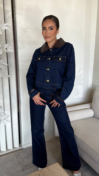Model wearing a dark wash denim jacket and high rise jeans with button-up closure and 5-pocket style.
