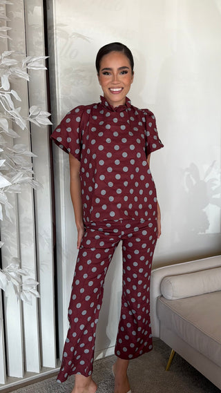 Polka dot ruffle top and flare crop pant set in maroon worn by a smiling model.