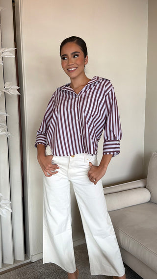 A woman wearing a striped long sleeve shirt with a relaxed fit and button-down front, paired with white pants.