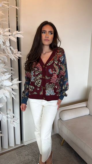 A woman wearing a multicolor floral knit cardigan with a buttoned front and burgundy accents.
